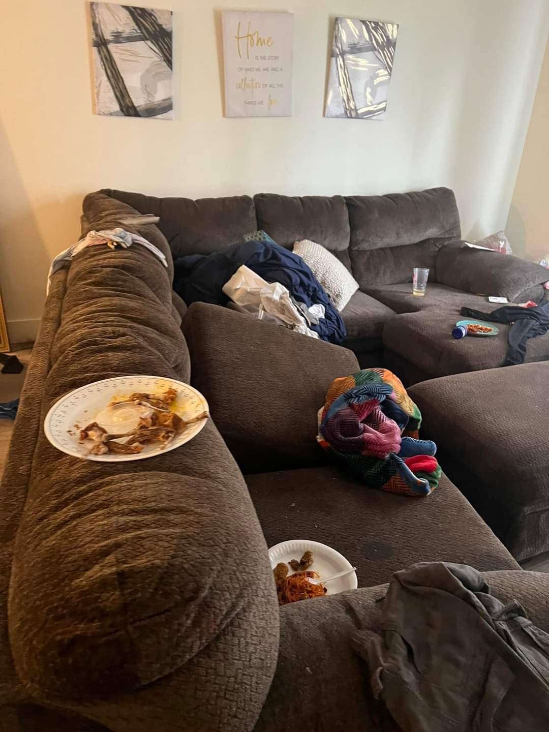 Living room with a cluttered brown sectional sofa, scattered with plates, clothes, and bags. Wilk's Junk Service handled the apartment cleanout.