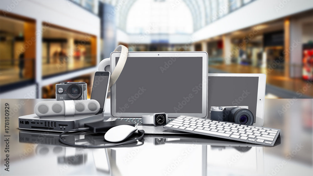 Various electronic devices, including a desktop with dual monitors, a laptop, a tablet with a stylus, a smartphone, headphones, and speakers, arranged on a reflective surface. Wilk's Junk Service handled the recycling.