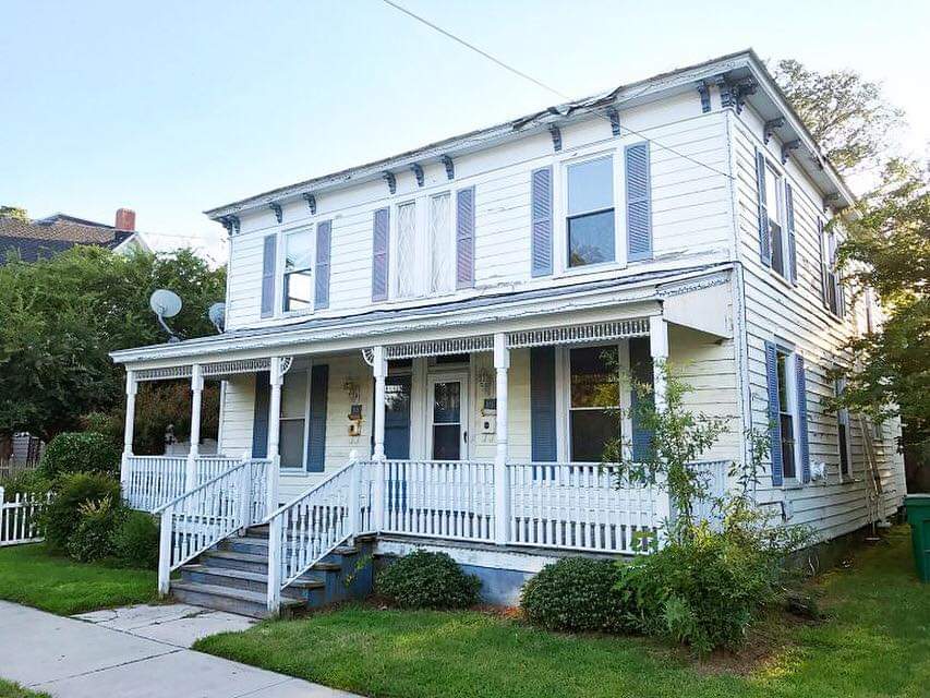 A two-story house with white siding and blue trim, featuring a covered front porch and well-maintained lawn. The photo was taken prior to the estate cleanout by Wilks Junk Service.