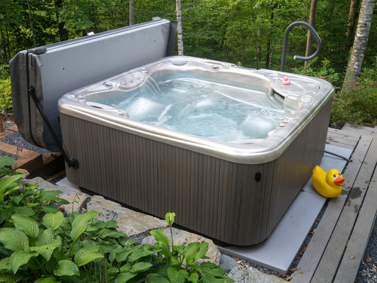 A hot tub with a gray cover sits in a stone and grassy area. A big rubber duck is on the right side. Wilk's Junk Service picked it up.