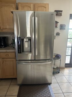 Stainless steel French door refrigerator with a bottom freezer, ice and water dispenser on the left door. Surrounded by wooden cabinets, black countertop, and tiled floor. Wilk's Junk Service hauled it away.