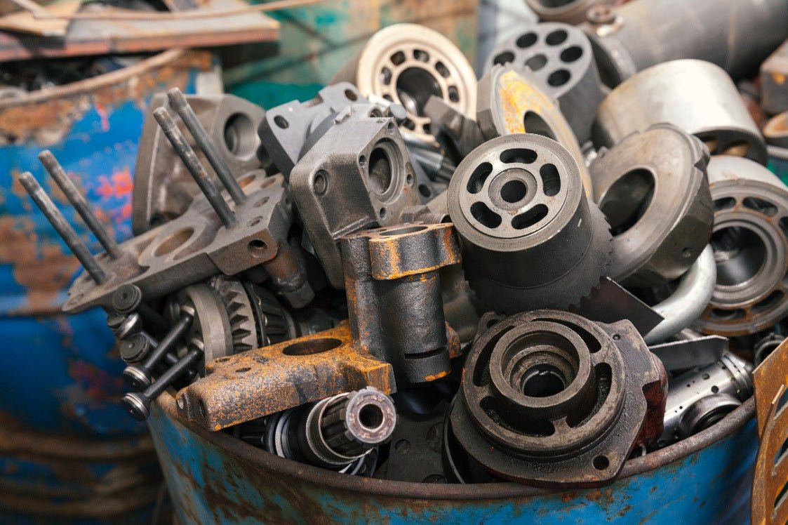 A collection of worn and rusted metal parts, including machinery components, gathered in and around a blue barrel. Cleared out by Wilk's Junk Service.