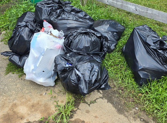 Multiple sealed black garbage bags piled on dirt and grass, ready for collection. Showcasing Wilk's Junk Service's expertise in waste management.